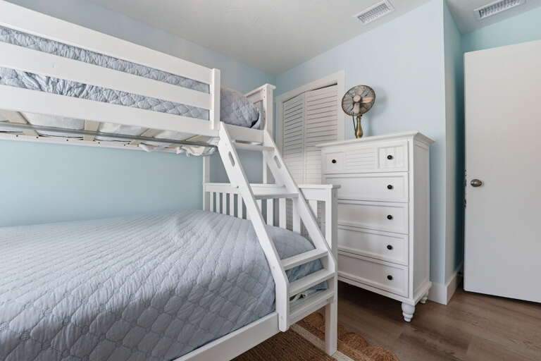 Pack the kids in the bunk room — twin over queen, chest of drawers, light blue walls, and a vintage fan for that island feel.