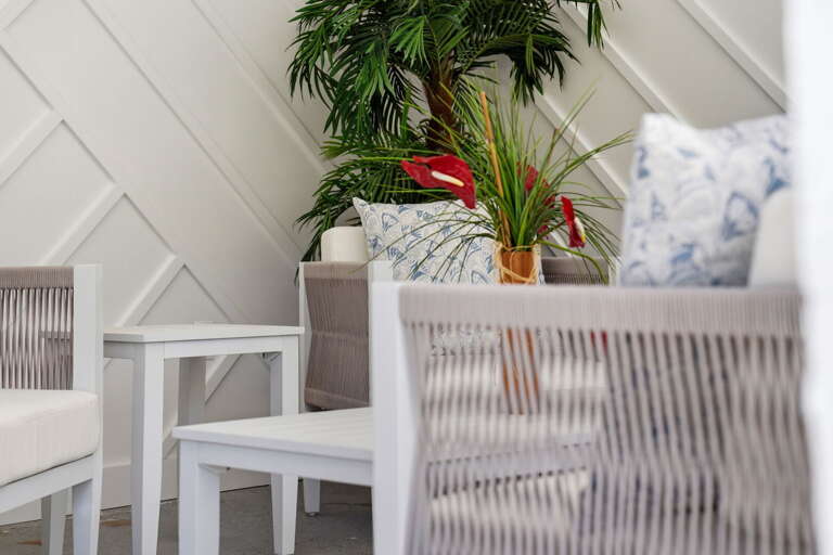 Pull up a wicker chair on the covered porch and stay awhile — colorful pillows, tropical potted plants, and an angled ceiling above.