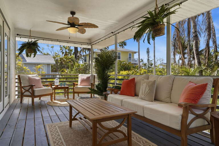 Settle into the screened porch sofa with your morning coffee — coral pillows, ceiling fan overhead, palms just beyond the screens.