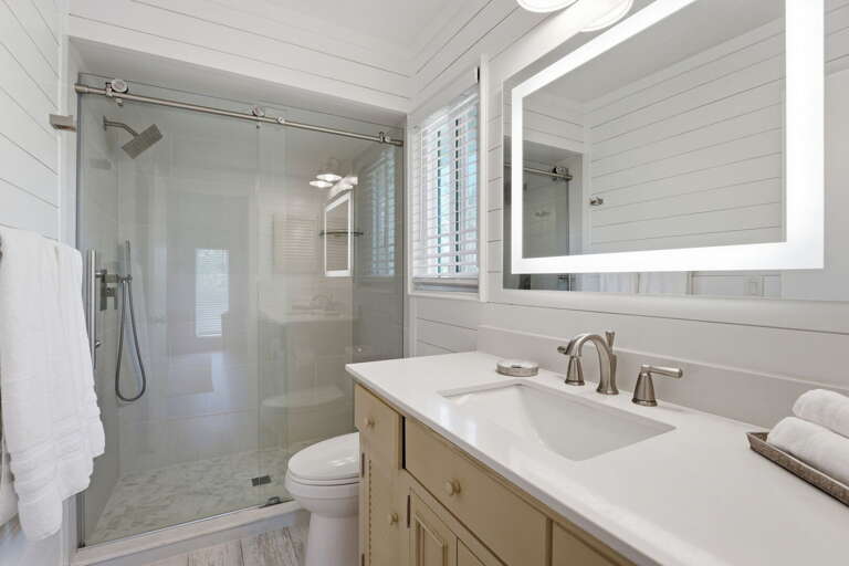 Start your mornings right in the master ensuite — glass walk-in shower, backlit mirror, white quartz countertop, and shiplap walls.