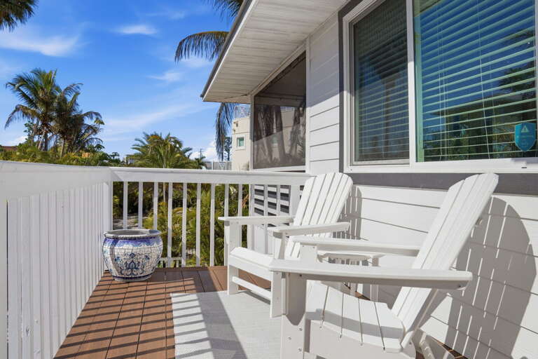 Steal a quiet moment on the second-floor balcony — two white Adirondack chairs, a potted plant, and palm views through the railing.