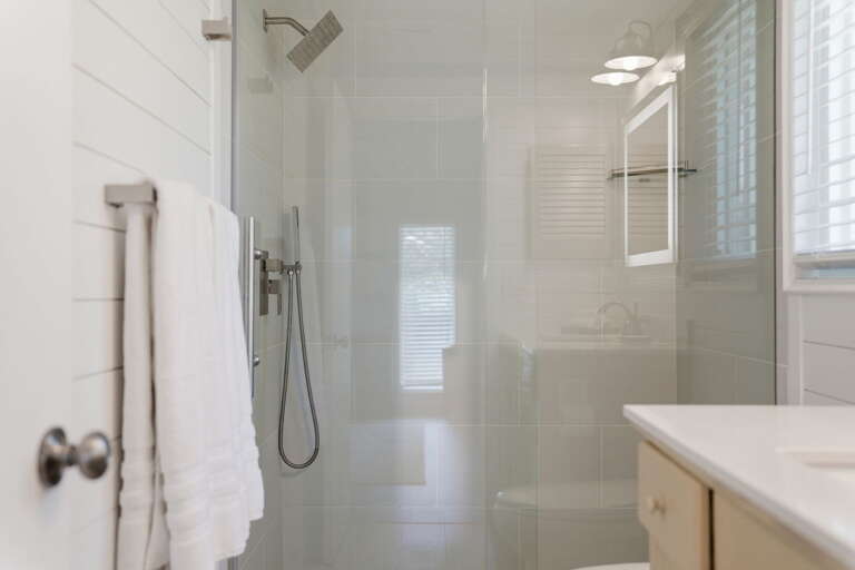 Step into the rainfall shower and take your time — handheld wand, white tile walls, and the towel bar right at the glass door.