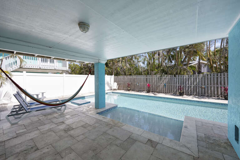 Hang in the hammock with the pool in view, covered patio keeping the afternoon heat off. Your do-nothing hour — take it.