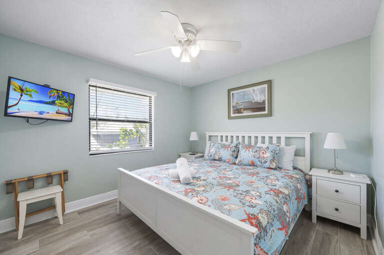 Your room for the week — coastal decor, wall-mounted TV, ceiling fan. Quiet enough to actually sleep in, even on the island.