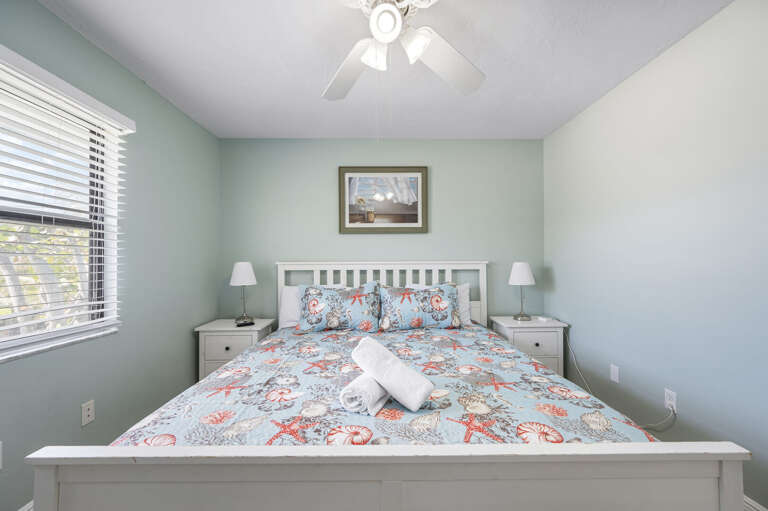 Your room for the week — coastal decor, wall-mounted TV, ceiling fan. Quiet enough to actually sleep in, even on the island.