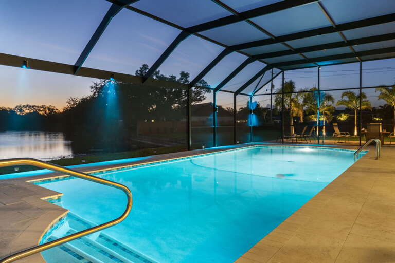 Your last cold drink of the night — lights low, pool glowing blue, lake just past the screen. This is the one.