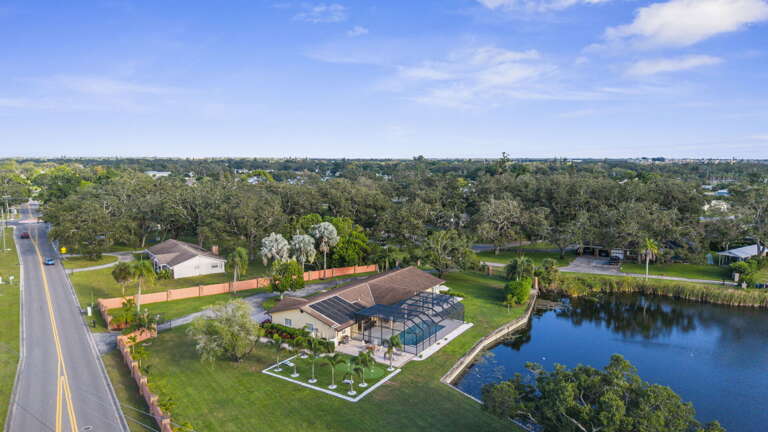 Your full acre from altitude — pool, green, home, lake, trees, and nothing crowding any of it.