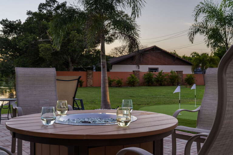 Pour the wine, light the fire-pit table, putting-green flag waving past the flame — outdoor dinner the way it should be.