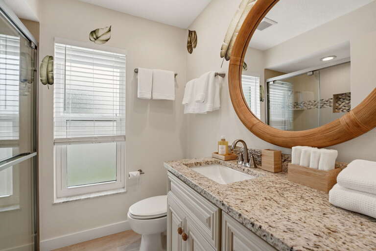 The second bathroom brings it all together — rattan mirror, walk-in glass shower, and tropical leaf decals that feel collected, not staged.