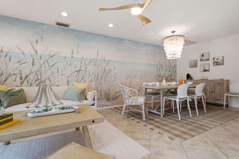 The full mural stretches from floor to ceiling — palm trees, white sand, the whole scene — with the dining table and sofa in front of it.