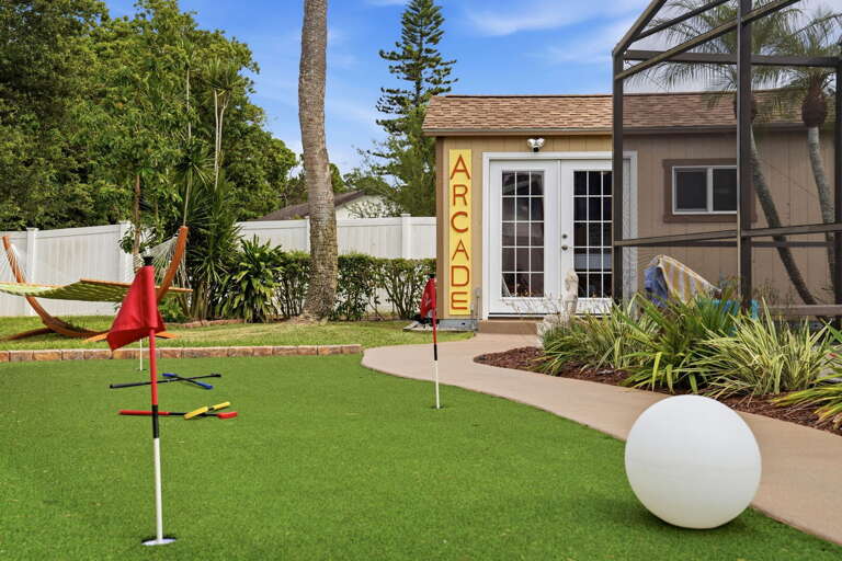 Putting green with two flags, a hammock between the palms, and the ARCADE building behind it. Your backyard has more going on than most parks.