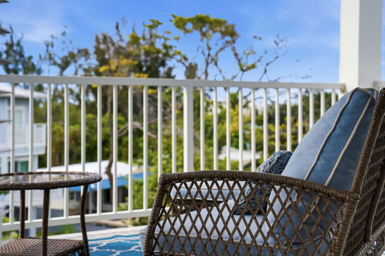 Balcony detail - a cushioned wicker loveseat with blue and patterned throw pillows invites you to sit back and soak in the Florida sky and water views.