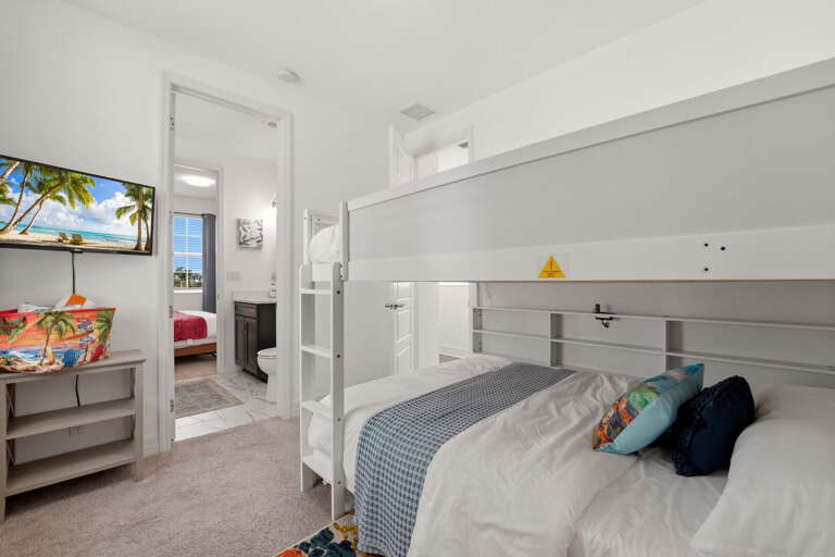 The bunk room is a kids' paradise - queen-over-queen bunk beds with built-in ladder, wall-mounted TV, colorful tropical rug, and its own bath access.