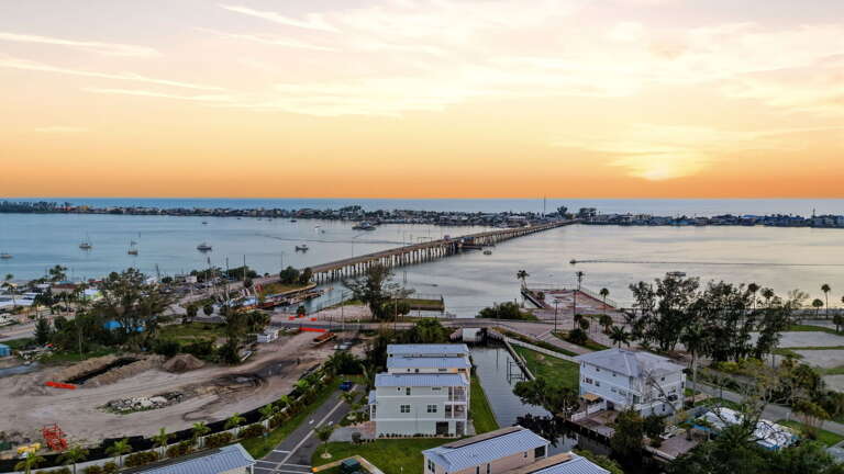 Drone view captures the full coastal picture at sunset - the property is prominently situated just steps from the bay, with the Cortez Bridge piers visible