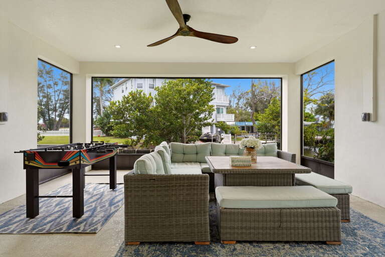 The ground-floor enclosed lanai is an entertainer's dream - a full wicker sectional with plush cushions, foosball table, ceiling fan,