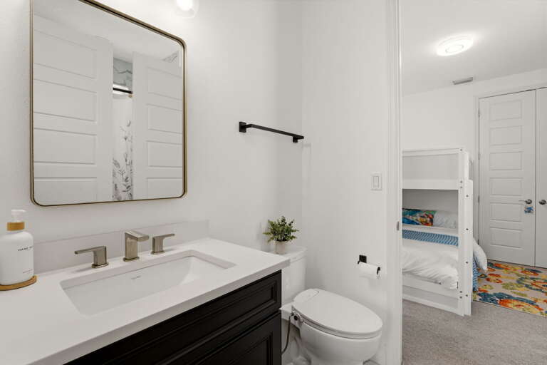 The jack-and-jill bathroom features a dark cabinetry vanity with quartz countertop, gold-framed square mirror, and a shared shower/tub area connecting both bedrooms.