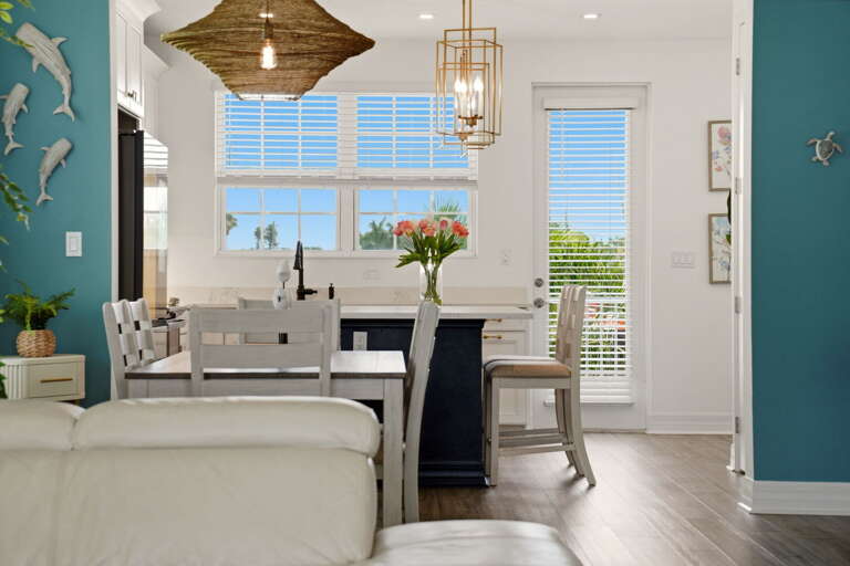 The kitchen and dining transition zone is framed by the statement rattan pendant and gold lantern lights, with the navy-and-white kitchen as a stunning backdrop.