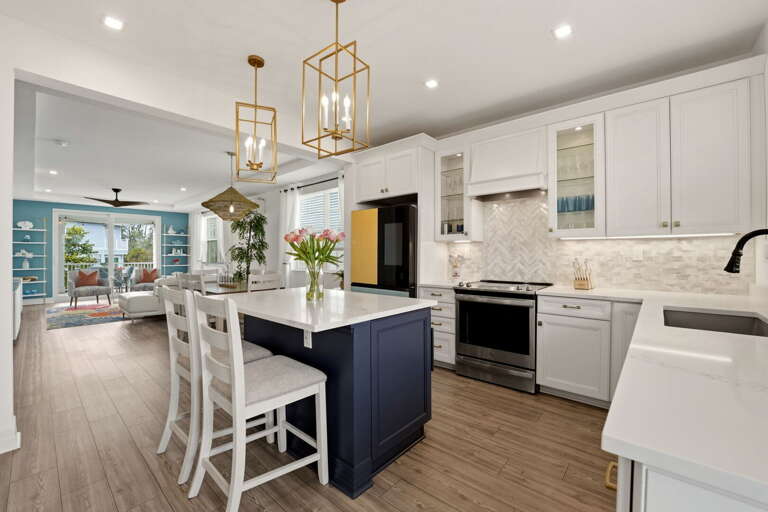 The kitchen opens beautifully to the dining and living areas - gold lantern pendants, white cabinetry, and the deep navy island