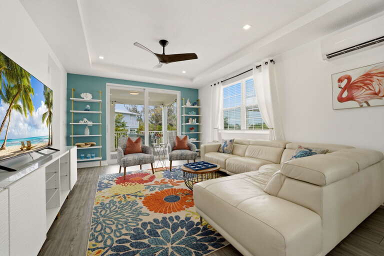 The main-level living room impresses with soaring ceilings, filled with coastal decor, a large flat-screen TV, and a vibrant tropical area rug.