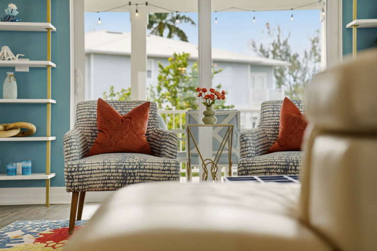 A pair of stylish accent chairs with rust-orange pillows frame the French doors perfectly, with bistro string lights twinkling on the balcony just beyond.