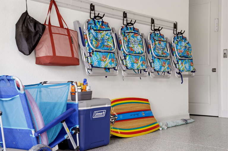Everything you need for a perfect beach day lives right here - wall-mounted beach chairs, a Coleman cooler, and colorful boogie boards
