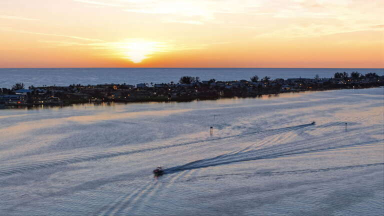 Pure Florida magic - a lone boat traces its path across the glass-smooth surface of Sarasota Bay as the sun sinks below the horizon.