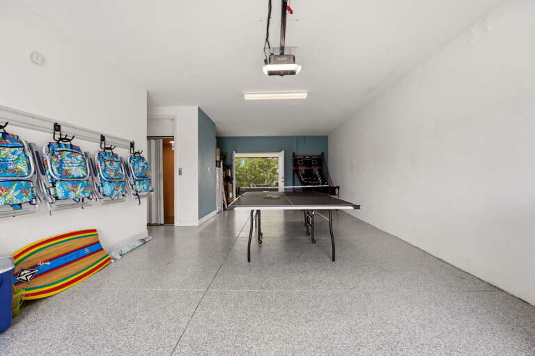 The ultimate beach-ready garage doubles as a game room, featuring a ping pong table, basketball arcade game, and all the beach gear needed