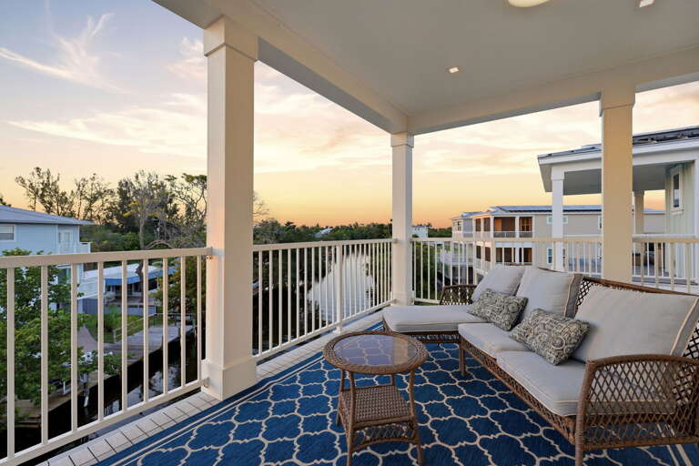 The upper back balcony is its own private escape - a wicker sofa with cream cushions and a small round glass table overlook the rooftops