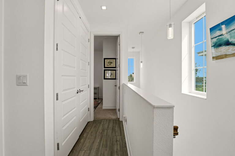 The upper hallway from the opposite direction, showing the staircase, closet doors, and the clean, light-filled layout of the second floor.