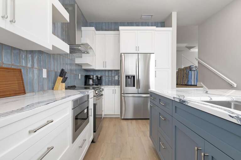 See the full run of lower cabinets and the island with bar stools from this angle — fully stocked and easy to navigate, it's a working kitchen that keeps up with a large group.