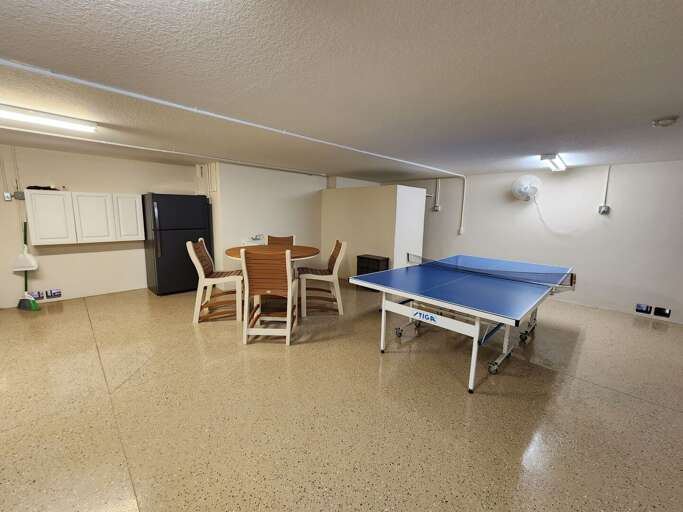 Your ground-floor game room spans the full width of the house — ping pong, darts, round dining table, black fridge stocked and ready. Plans for the night start here.
