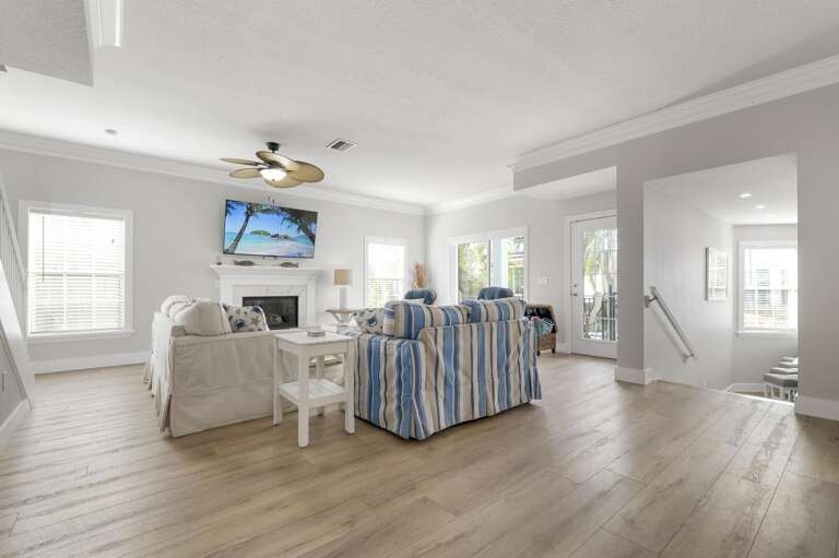 Your main living room opens wide — palm-blade ceiling fan overhead, TV mounted above the fireplace, and enough seating for the whole group without anyone getting squeezed.