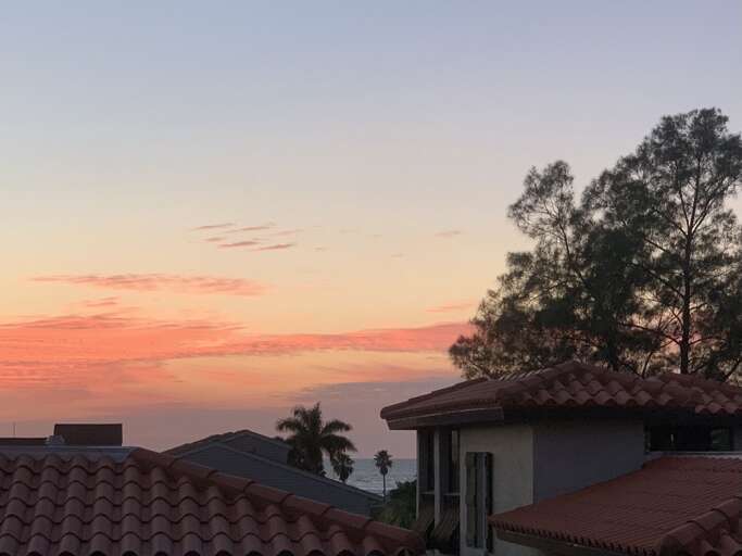 You're on the rooftop when the sky does this to Anna Maria Island — orange and pink burning over the rooftops. This is why people book return visits before they leave.