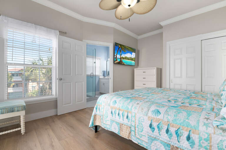 Slip away into the teal seashell quilt, hit the wall TV, and step out to the balcony when you want air — this queen bedroom is easy to disappear into after a full day.