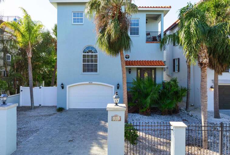 Spot the light blue three-story stucco from the street and you're there — the white garage door, the landscaping, and the size of it all make arriving here feel like a moment.