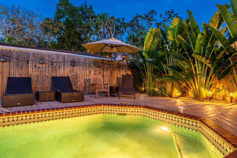 Grab your lounger before someone else does — three chairs poolside, an umbrella overhead, and a pool that glows once the sun drops.