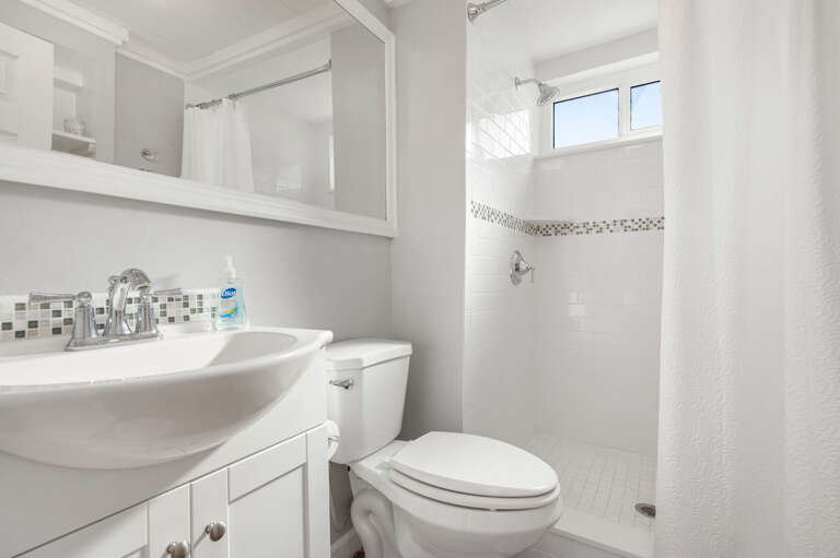Step into the clean white bathroom: mosaic tile backsplash, pedestal sink, walk-in shower with actual room to move. Bright enough to make the morning routine feel like part of it.