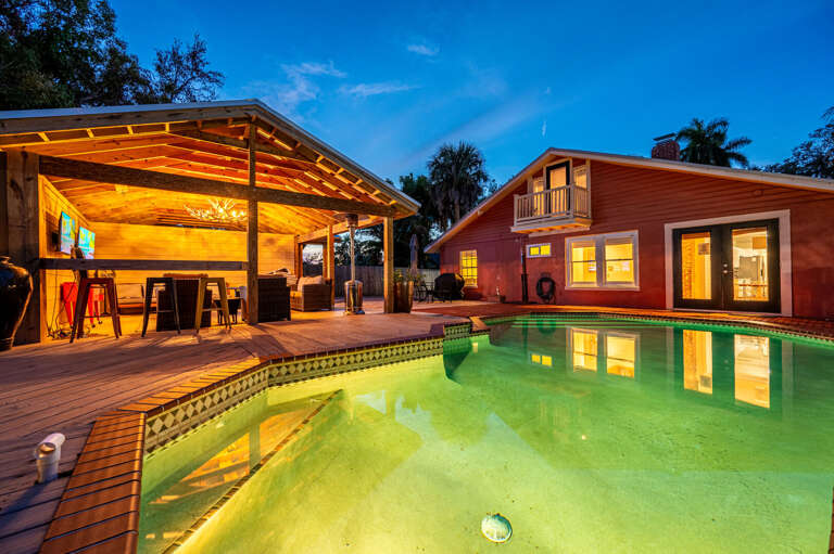 Step back and take it in — the back of the house at dusk with the pool glowing, the cabana lit, and the coral walls catching the last of the light.