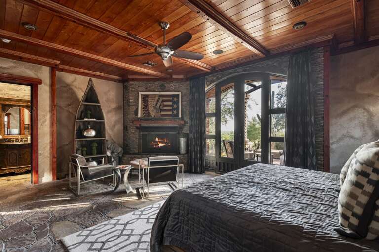 Retreat to this luxurious bedroom featuring a cozy fireplace, elegant wood finishes, and a private p