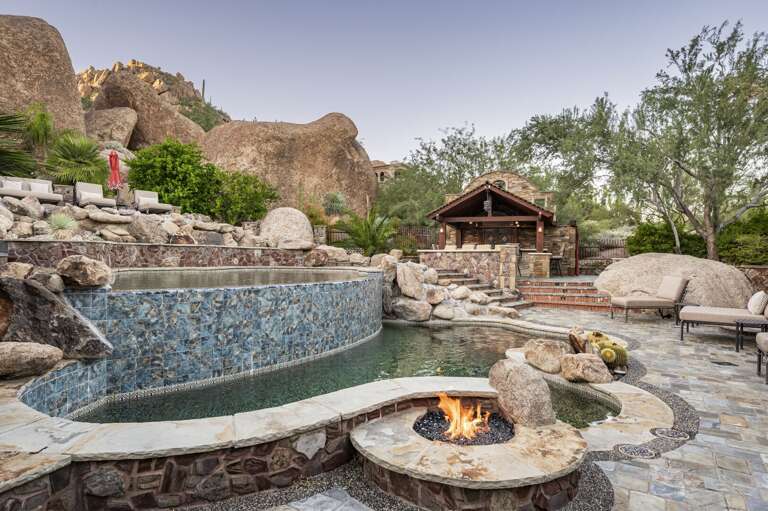 Enjoy resort-style relaxation with a cascading pool, cozy fire feature, and stunning natural boulder backdrop.
