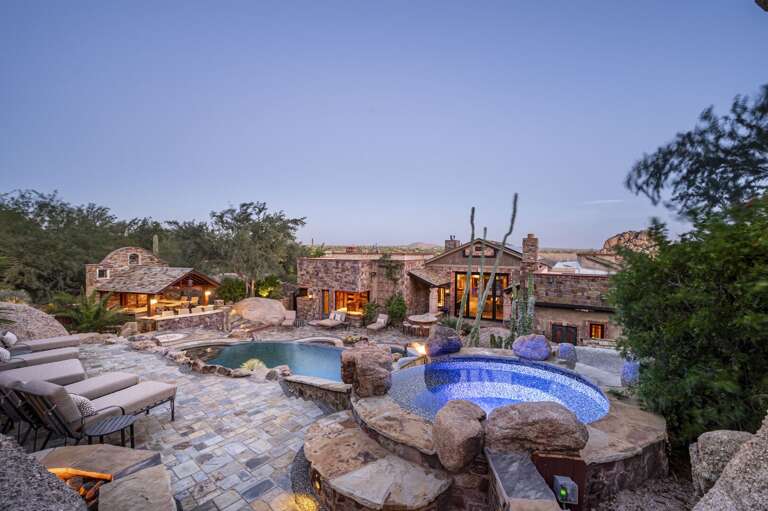 Enjoy unforgettable desert evenings with a sparkling pool, cascading waterslide, cozy outdoor fireplace, and breathtaking boulder views.