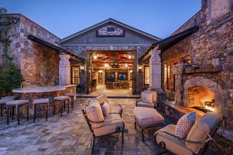 Unwind in this elegant outdoor retreat, where plush seating, a grand stone fireplace, and warm evening lighting create the perfect atmosphere for relaxing and gathering under the desert sky.