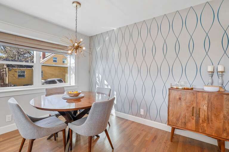 The adjoining dining area features a table and chair set for four, perfect for enjoying meals together under a golden, starburst chandelier. The adjoining dining area features a table and chair set for four, perfect for enjoying meals together under a golden, starburst chandelier.