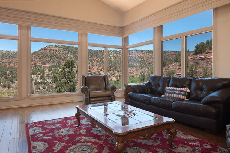 The inviting living room offers ample seating with a leather sofa, large flat-screen TV, and floor-to-ceiling windows framing stunning panoramic views of the Sedona landscape. The inviting living room offers ample seating with a leather sofa, large flat-screen TV, and floor-to-ceiling windows framing stunning panoramic views of the Sedona landscape.