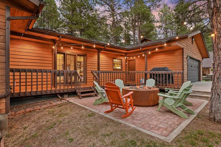 Cozy cabin patio with string lights, fire pit, Adirondack chairs, and surrounded by tall pines—perfect for relaxing evenings. Cozy cabin patio with string lights, fire pit, Adirondack chairs, and surrounded by tall pines—perfect for relaxing evenings.