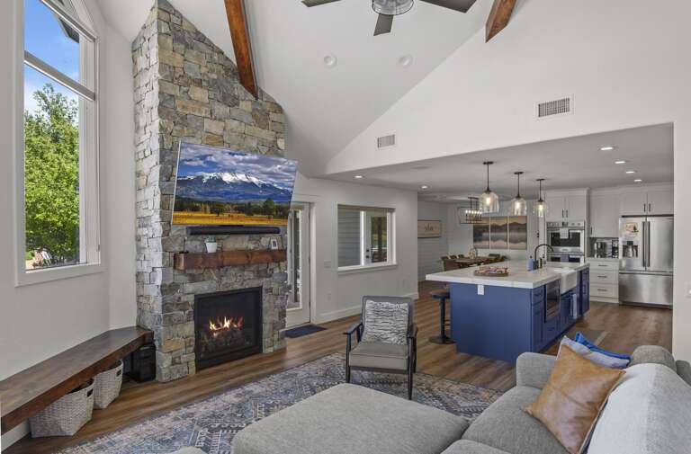 A stone gas fireplace anchors the room, surrounded by a plush L-shaped couch, a chaise lounge, and a wall-mounted TV. A stone gas fireplace anchors the room, surrounded by a plush L-shaped couch, a chaise lounge, and a wall-mounted TV.