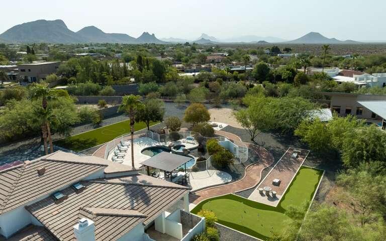 A breathtaking aerial view of the private backyard oasis with lush grounds, resort-style amenities, and stunning mountain views beyond.