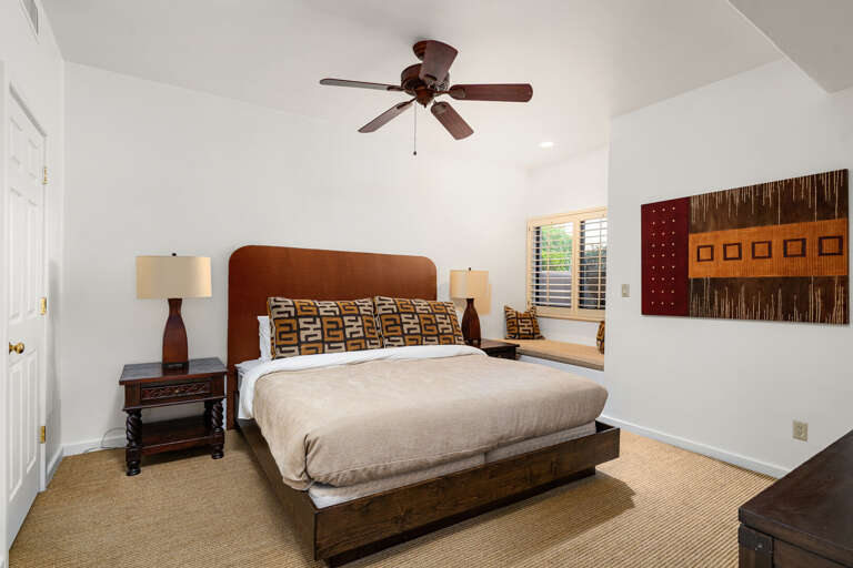 Comfortable second bedroom with plush bedding, ceiling fan, and a cozy bench seating area.