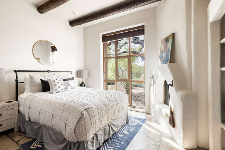 A bright and inviting guest bedroom with a comfortable queen bed, fireplace, natural light, and Southwestern-inspired charm for a restful stay.