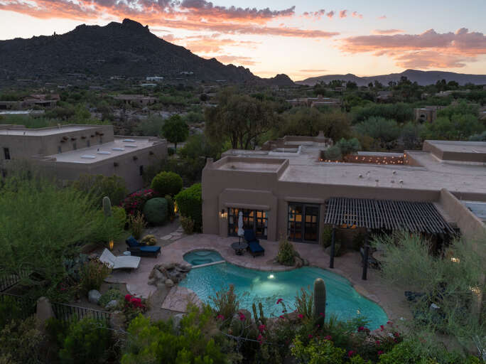 End the day with stunning aerial views of the illuminated pool, lush landscaping, and peaceful desert surroundings at sunset.